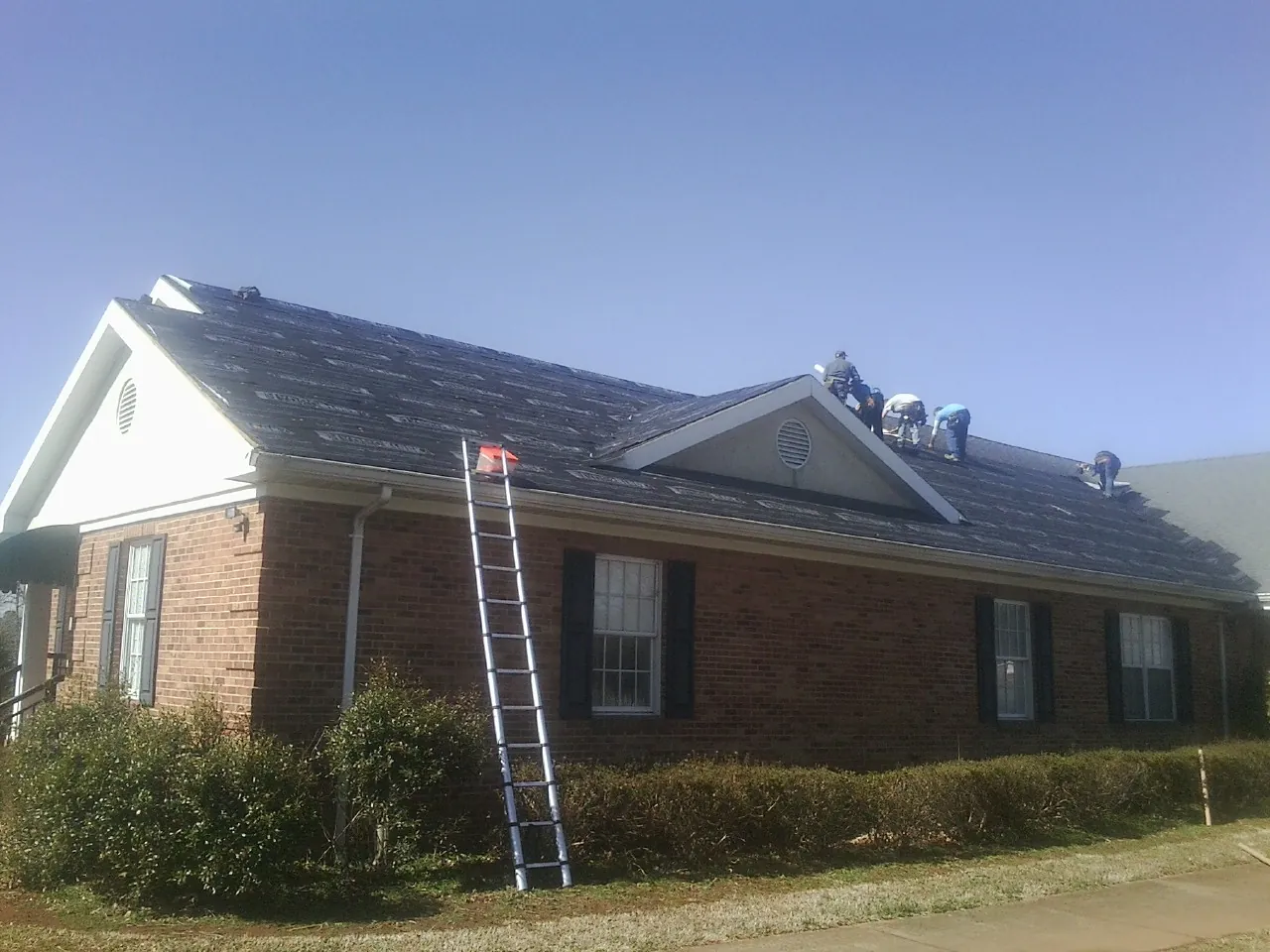 Crew tearing shingles off a brick ranch roof with a ladder set — Metal Roof Repair work by our crew in Griffith