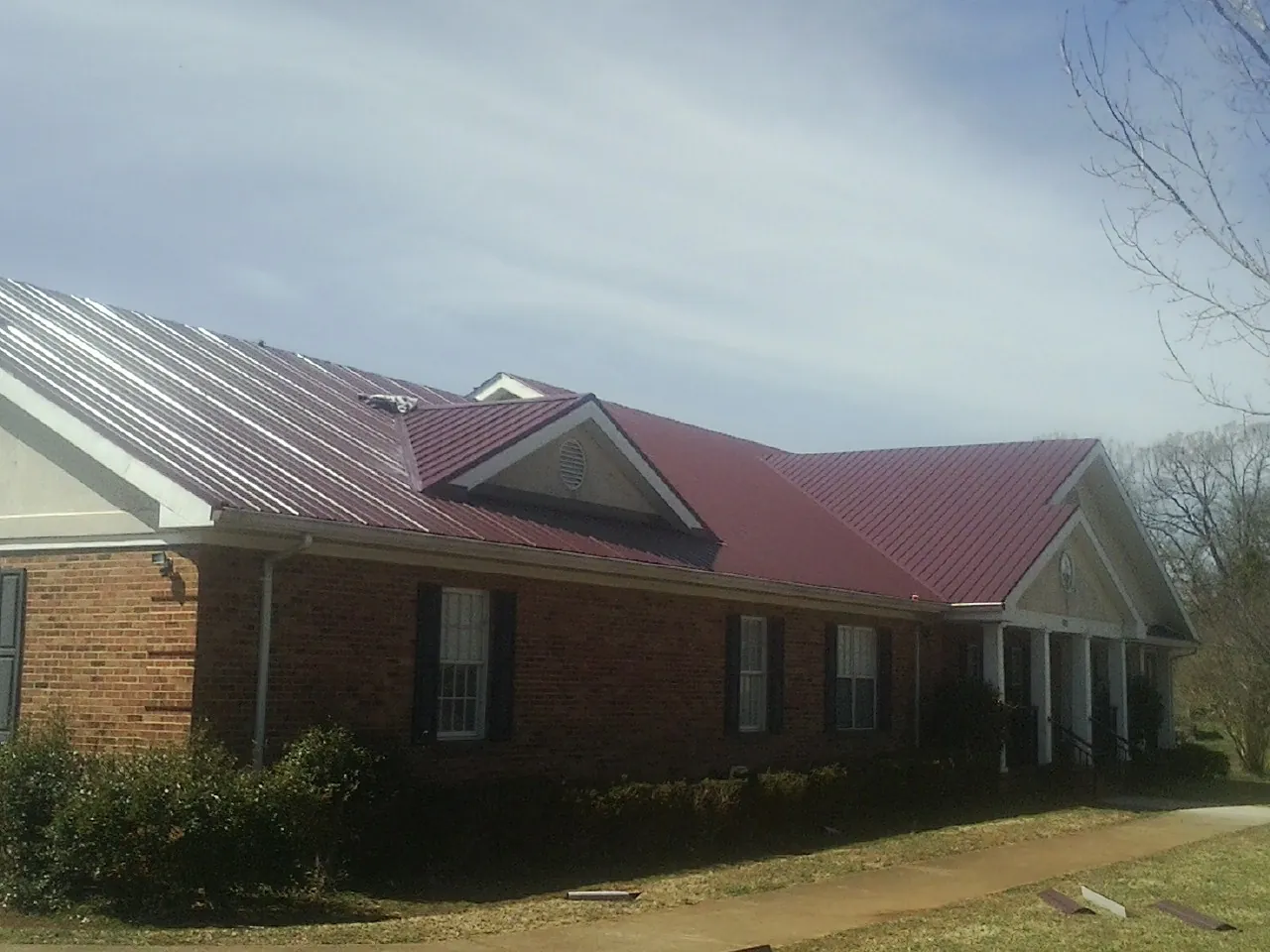 Red metal roof with gabled entries on a long brick building, from a Hail Damage Roof Repair job in Griffith