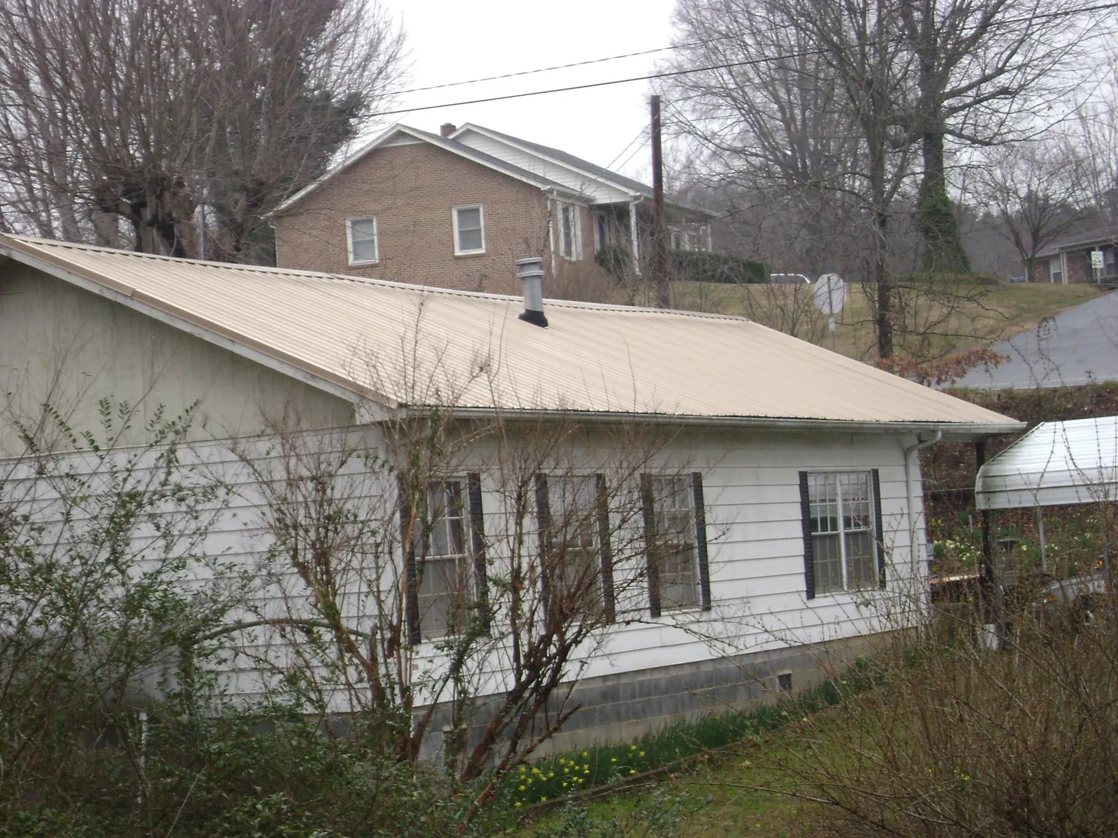 Tan metal roof on a white sided house set into a hillside — Commercial Roofing by Roofing Brothers in Griffith