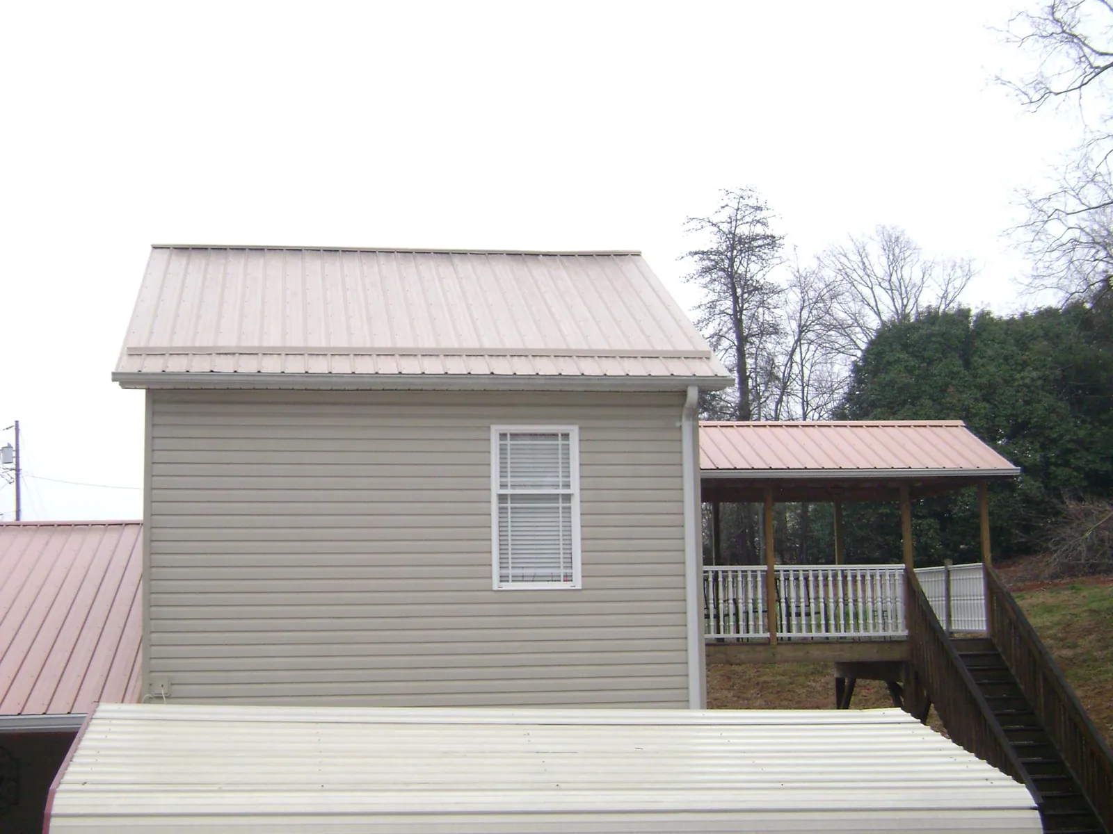 Tan metal roofs on a two story addition and attached porch, from a Roof Replacement job in Griffith